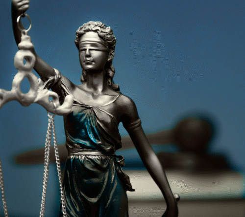 Figura Temidy z opaską na oczach i wagą w dłoni, symbolizująca sprawiedliwość, na tle młotka sędziowskiego i książek prawniczych.